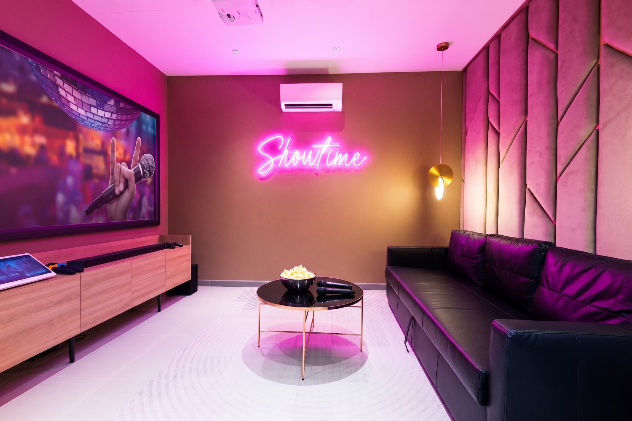 The KTV lounge of the Indigo wing — magenta-neon Showtime sign, 100-inch projector, popcorn and microphones on the coffee table.
